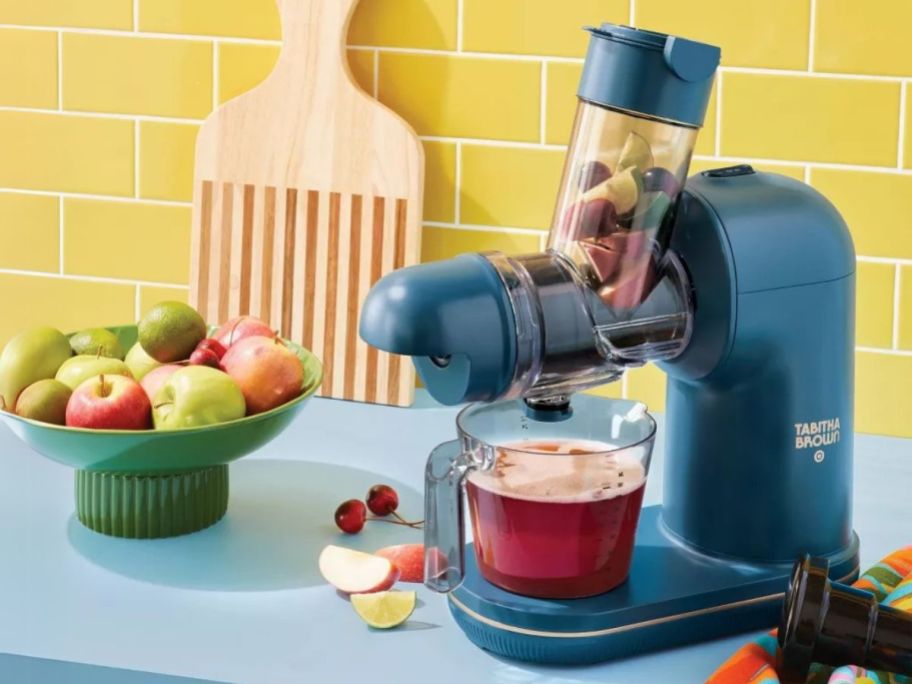Tabitha Brown Electric Masticating Juicer on counter with fruits next to it in a bowl