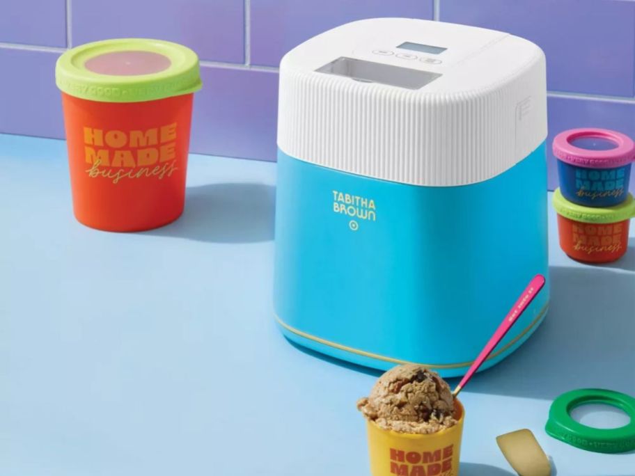 blue Tabitha Brown Electric Ice Cream Maker on counter with a scoop of ice cream in front of it