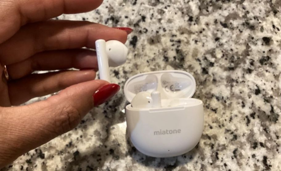 a womans hand holding a wireless earbud next to a charging case